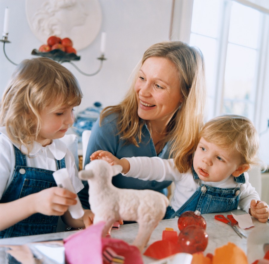 A mother with her daughter and son  making Christmas decorations together by a table full of arts and crafts tools.